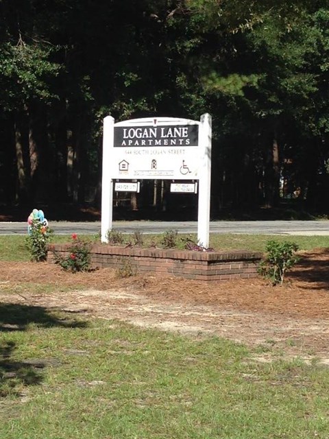 A sign for Logan Lane Apartments stands in front of a wooded area.