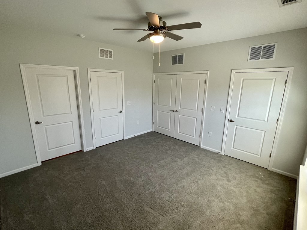 an empty living room with three doors and a ceiling fan