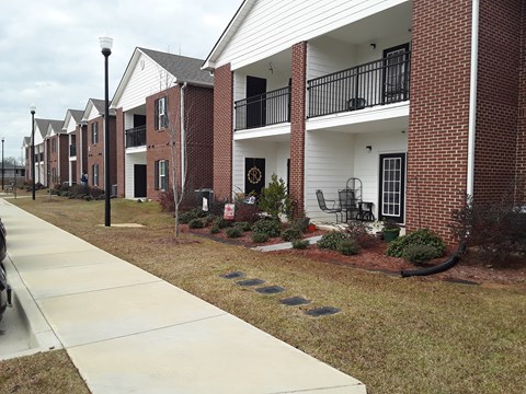 A row of red and white townhouses with a sidewalk in front.