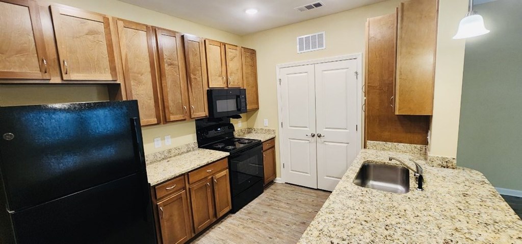 A kitchen with a black fridge, white cupboard, and a black stove.