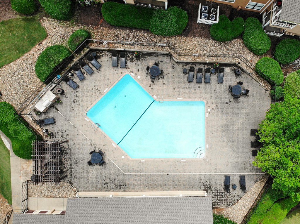 an overhead view of a swimming pool in a garden with tables and umbrellas