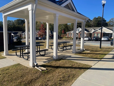 A white gazebo with black benches is in the foreground of a residential area.