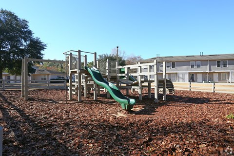 A playground with a green slide and brown leaves on the ground.