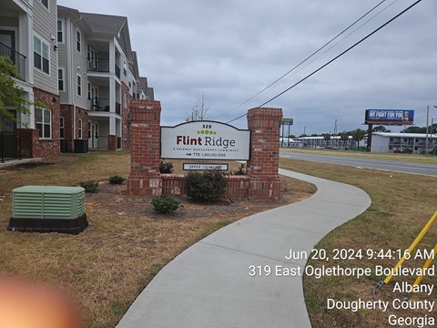 A sign for Flint Ridge Apartments is displayed in front of a brick wall.