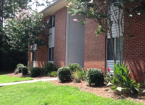 a side view of a brick building with a lawn and bushes