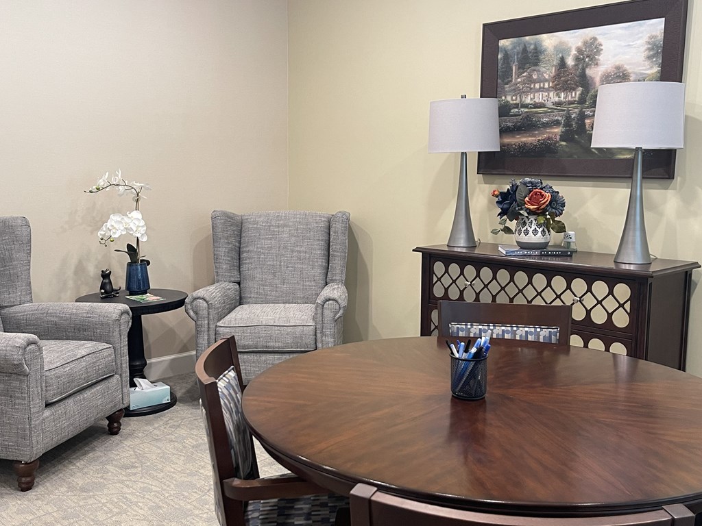 A living room with a grey couch, a grey chair, a wooden table and a painting on the wall.