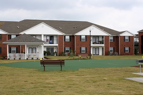 A large building with a white porch and a brown bench in front of it.