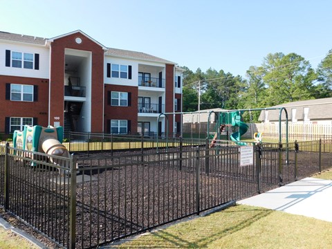 A playground with a black fence and a red brick building in the background.