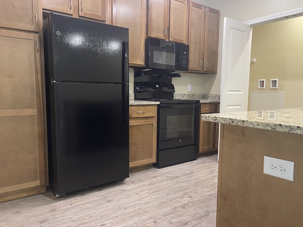 A black refrigerator is in a kitchen with wooden cabinets.