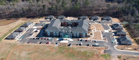 A large building with a green roof is surrounded by smaller buildings and a parking lot.