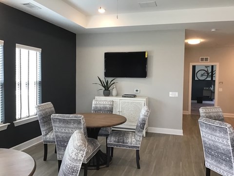 A conference room with a television mounted on the wall and a round table surrounded by chairs.