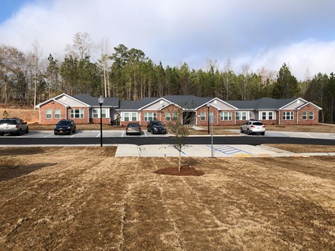 A parking lot in front of a building with a tree in the middle.