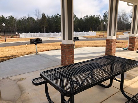 A black metal table is in front of a white fence and a brick pillar.