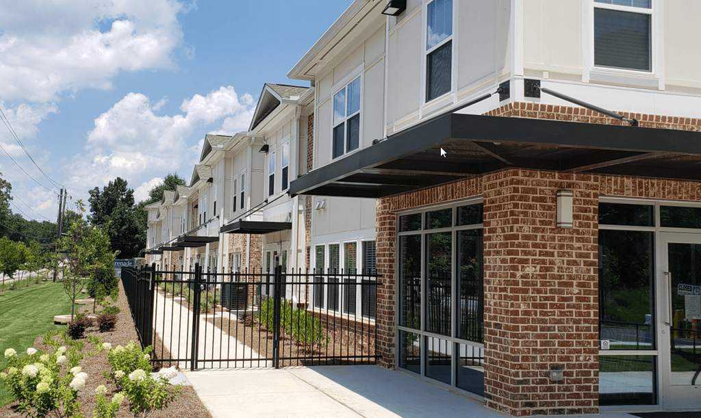 a row of apartment buildings with a sidewalk and a black fence