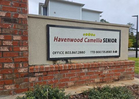 A sign for Havenwood Camellia Senior is mounted on a brick wall.