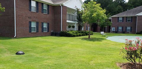 A grassy area in front of a brick building with a tree and a flower bed.