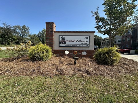 A sign for a Wood Elberton office is in front of a brick chimney.