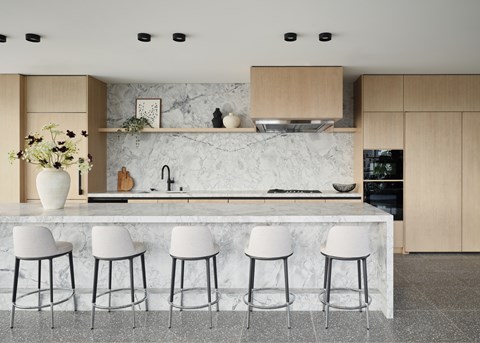 A kitchen with a marble countertop and white bar stools.