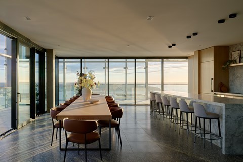 A dining room with a long table and chairs with a view of the outside.