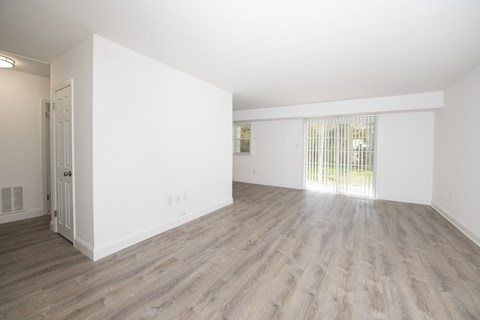 A room with white walls and wooden flooring with a door on the left.
