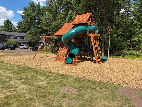 A playground with a green slide and a brown wooden structure.