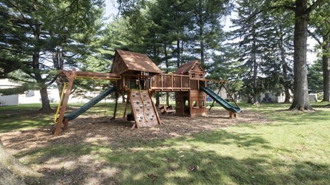 A wooden playground structure with a green slide and a yellow caution sign.