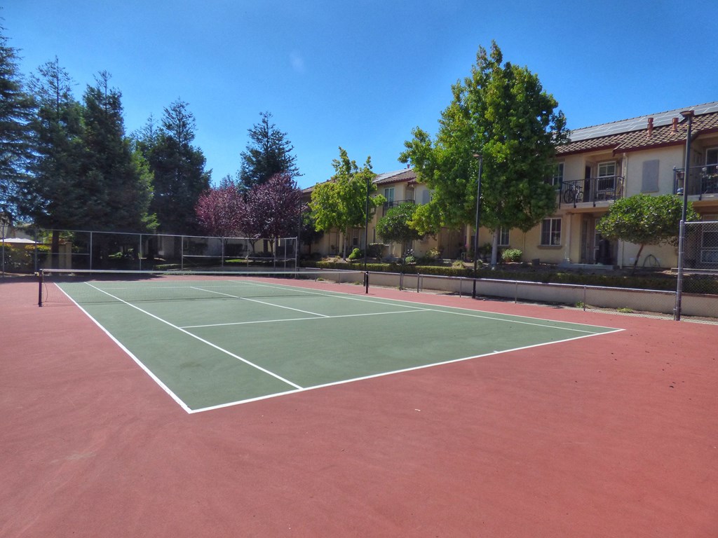 a tennis court in front of a building with trees