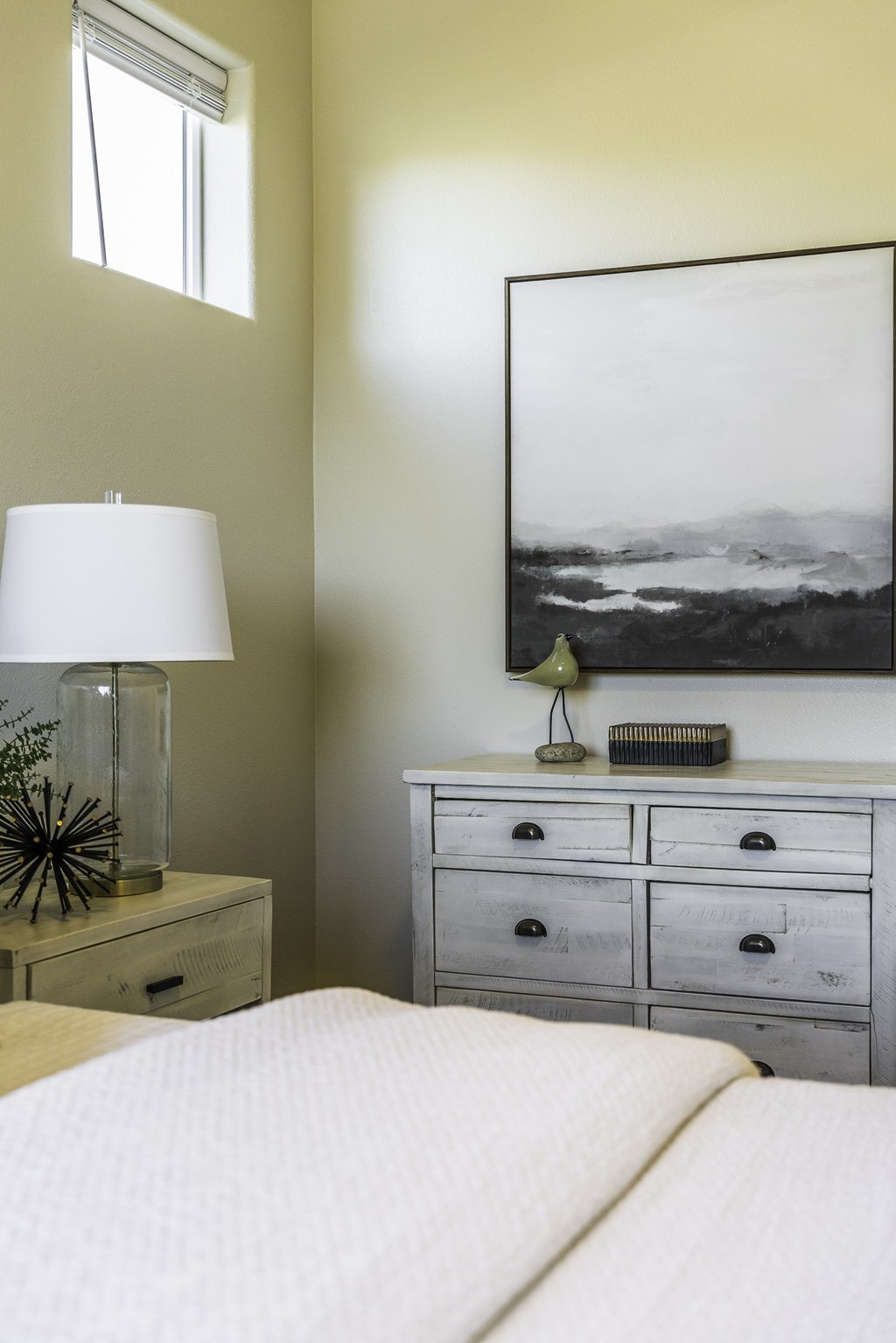 A bedroom with a bed, nightstand, and a large picture on the wall.
