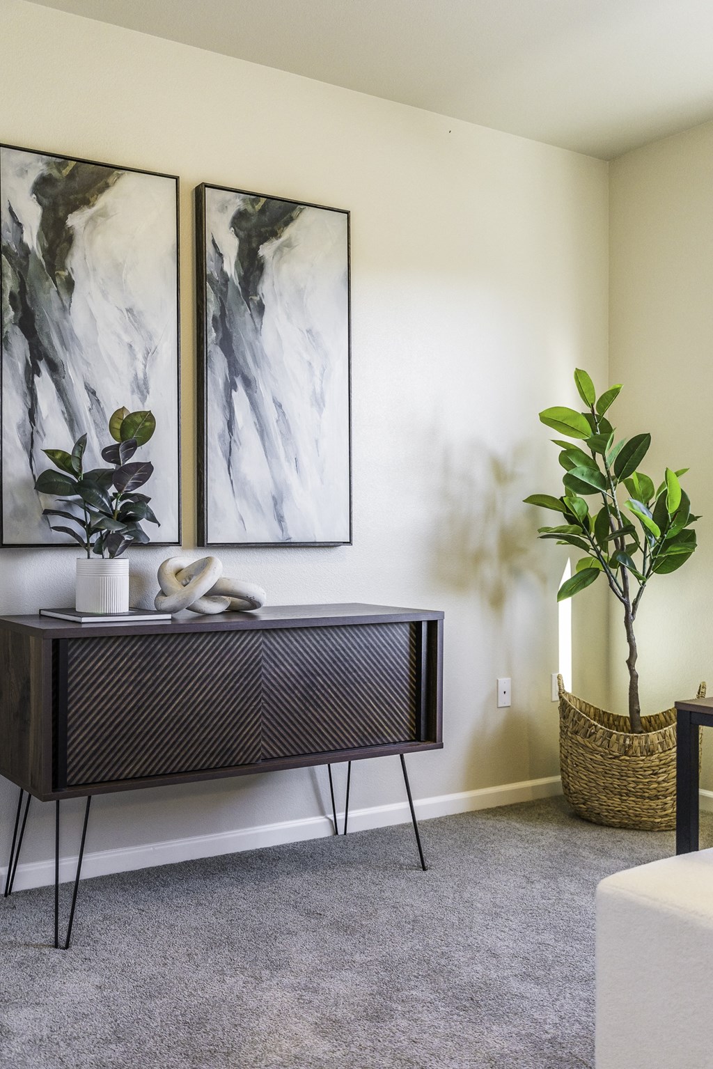 A room with a TV stand, two paintings, a plant, and a basket.