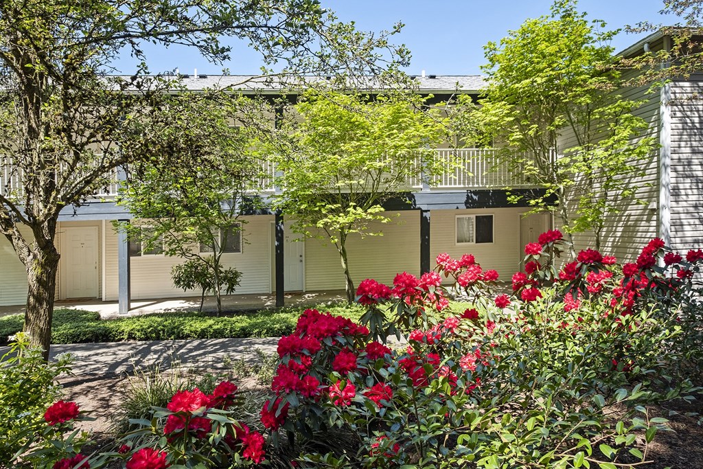 a garden with red flowers in front of a building at Mill Pond Apartments, Auburn, WA 98092