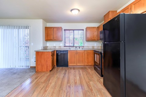 A black refrigerator is in the corner of a kitchen with wooden floors and cabinets.