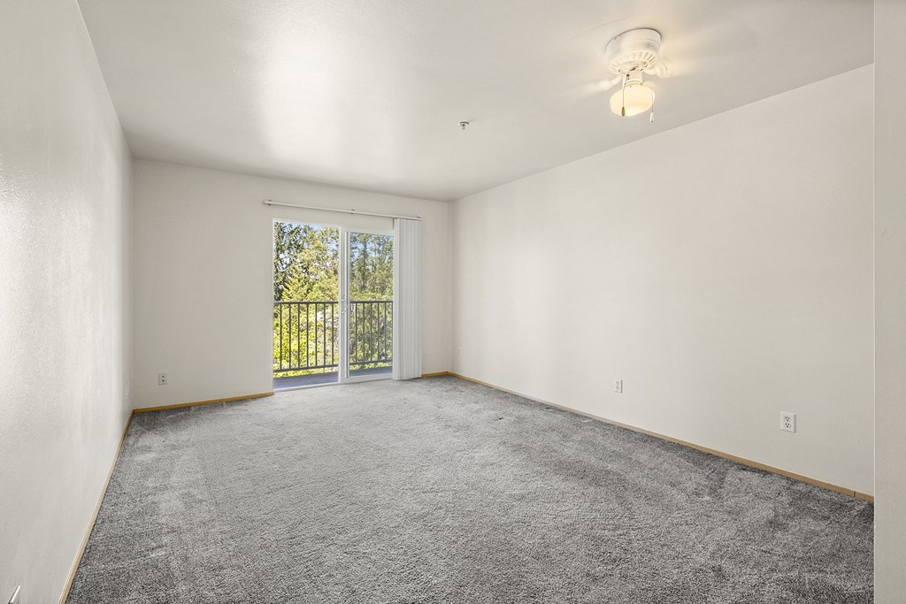 a bedroom with white walls and a sliding glass door to a balcony at Mill Pond Apartments, Auburn Washington