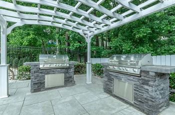 A patio with two stone BBQs under a white pergola at Crest at East Cobb Apartments, GA, 30062