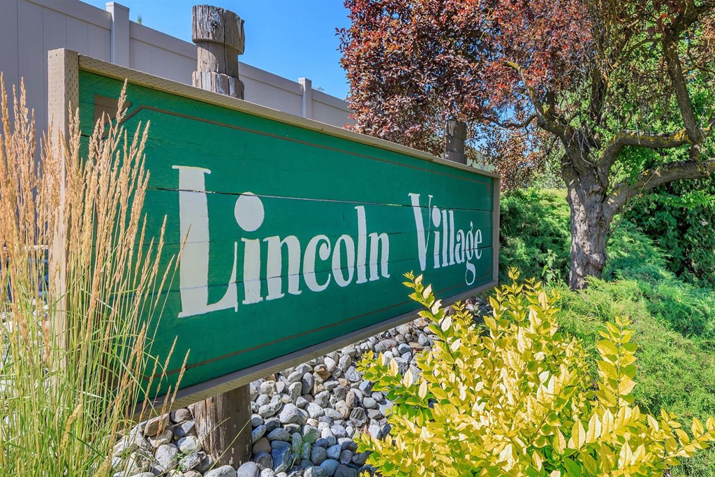 a green sign that says lincoln village with a tree in the background at Lincoln Village Apartments, Spokane Washington
