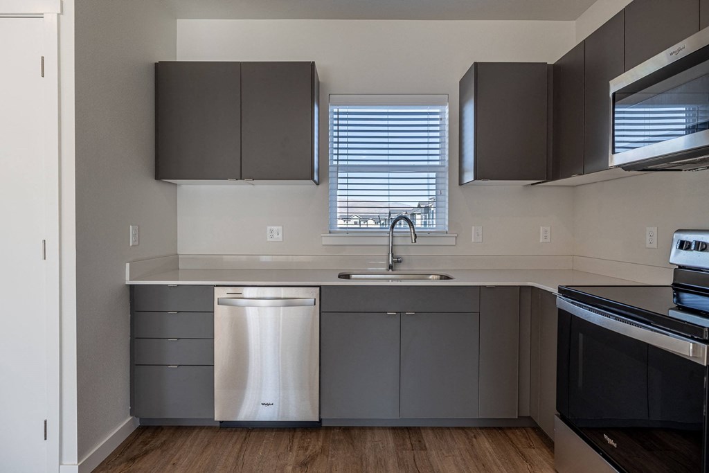 an empty kitchen with gray cabinets and stainless steel appliances and a window at Sagecrest Apartments, Wenatchee, Washington