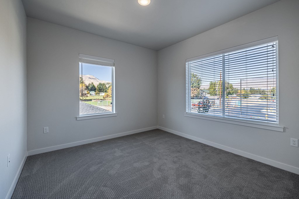 an empty living room with two windows and carpeting at Sagecrest Apartments, Washington, 98801