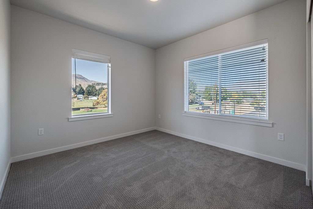 an empty living room with two windows and carpeting at Sagecrest Apartments, Washington