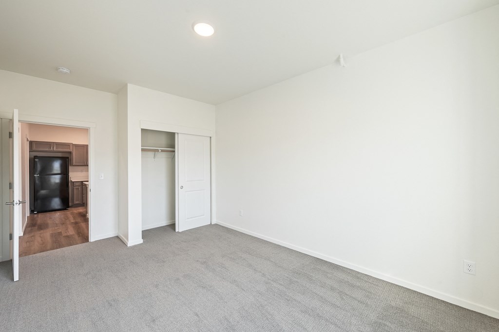 a living room with white walls and carpet and a door to a kitchen at Gateway Apartments, East Wenatchee