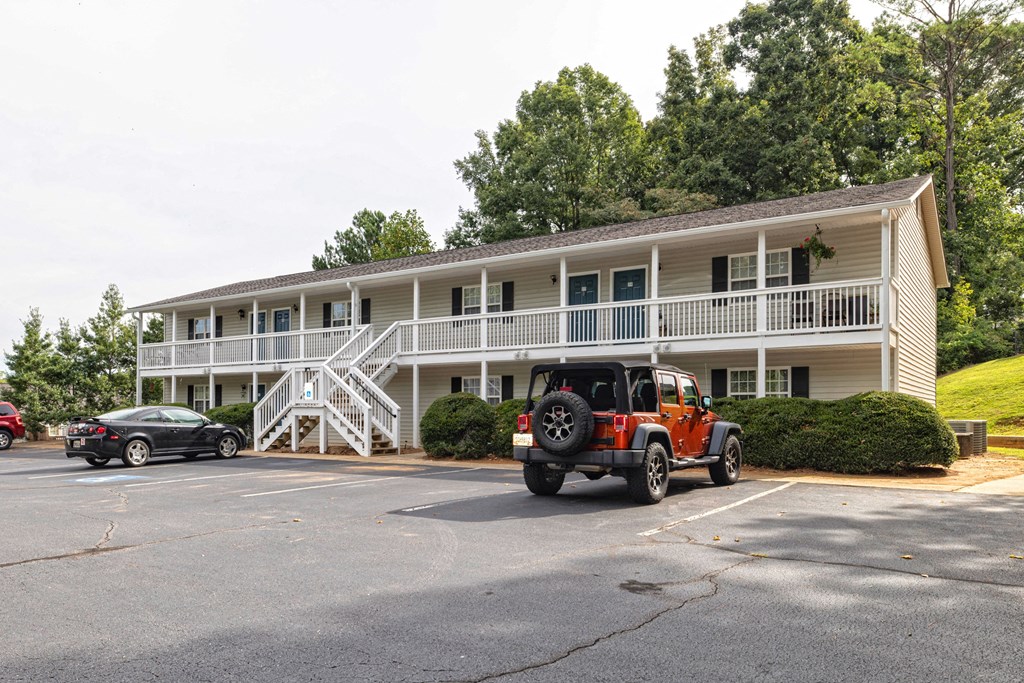 A red car is parked in front of a white building with a black car parked behind it at Overlook Club Apartments, Cummings