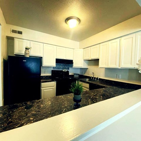 A black fridge and white cabinets in a kitchen.