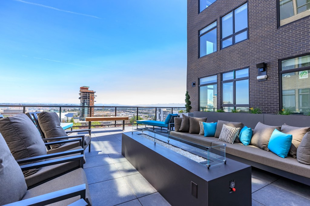 an outdoor patio with a firepit and lounge seating with a view of the city at Napoleon Apartments, Tacoma