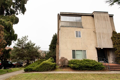 A beige building with a green bush in front.
