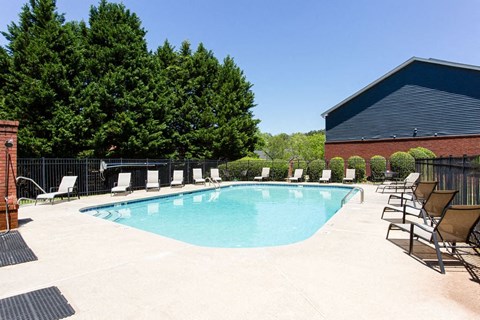 A pool surrounded by trees and chairs.