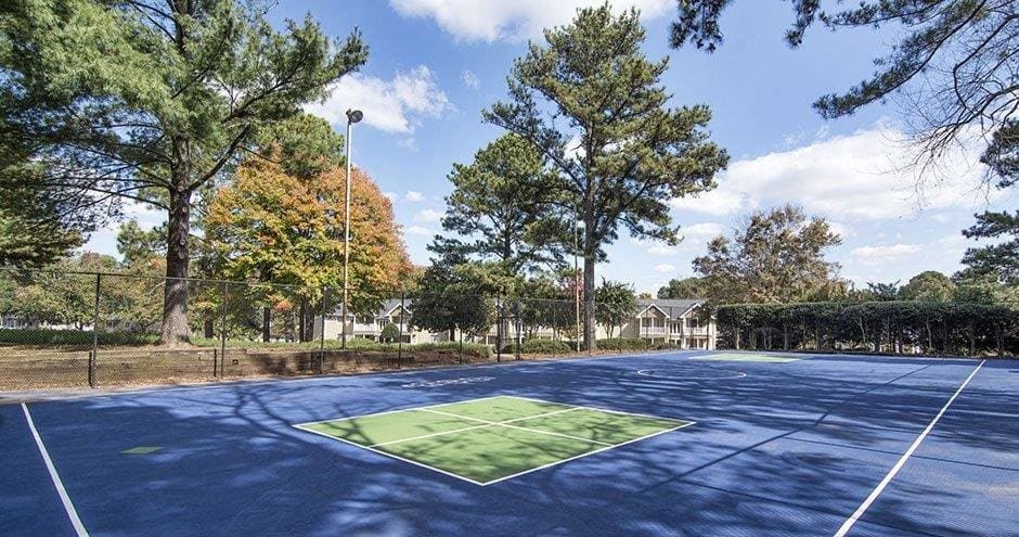 A tennis court surrounded by trees and a fence at The Madison Apartments and Townhomes, Georgia