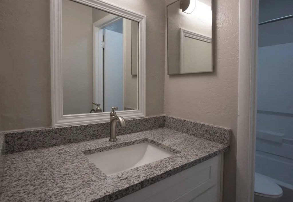A bathroom sink with a granite countertop and a mirror above it at The Madison Apartments and Townhomes, Lawrenceville, 30044