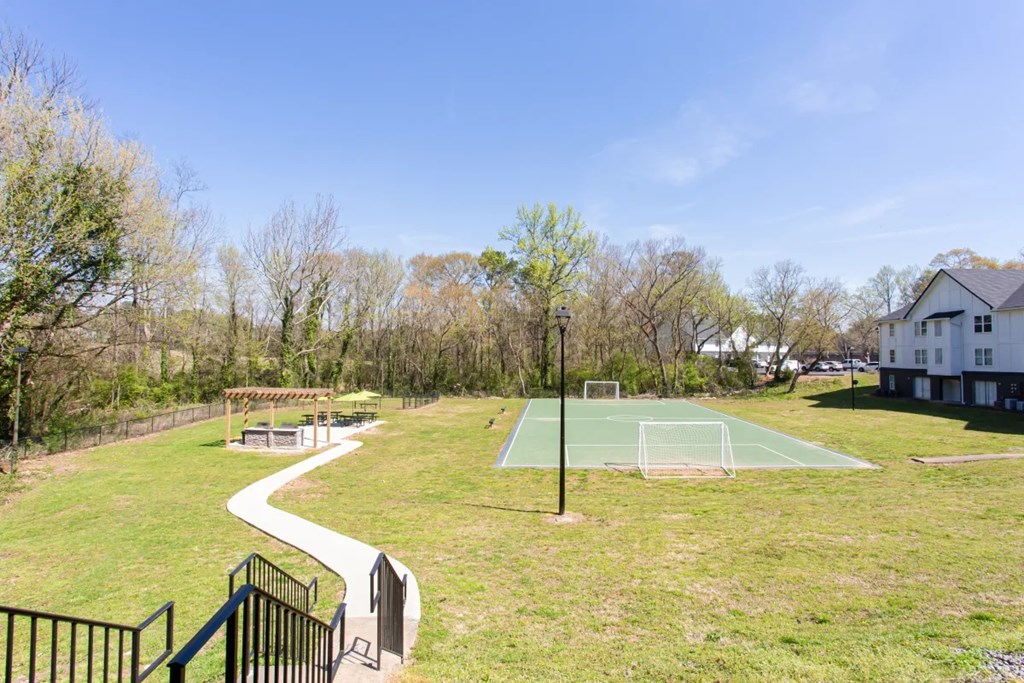 A green grassy area with a basketball court and a house in the background at Barcelo at East Cobb Apartments, GA, 30067