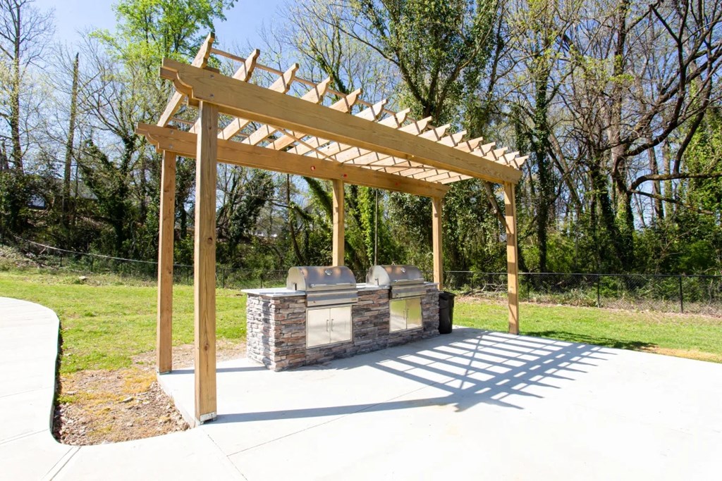 A wooden pergola structure is situated over a stone bench in a park at Barcelo at East Cobb Apartments, Marietta, GA