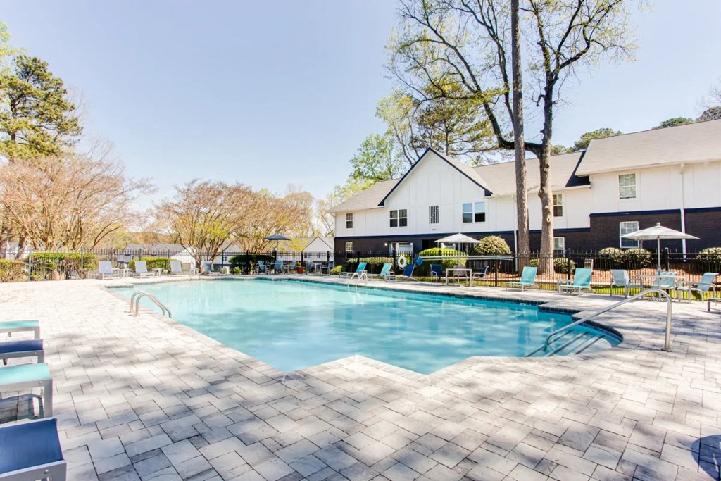 A large swimming pool surrounded by a tiled patio and a white house in the background at Barcelo at East Cobb Apartments, Marietta