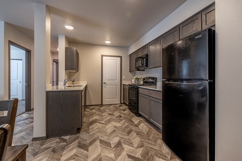 A black refrigerator is in a kitchen with a patterned floor.