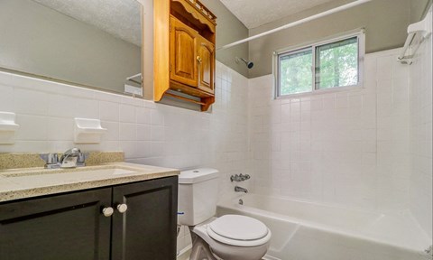 A white toilet sits in a bathroom with a white tub and a window.at Waverly Manor Townhomes, Norcross, GA